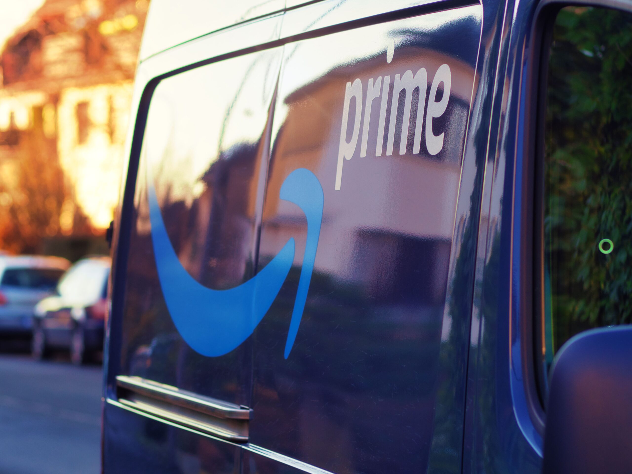 Close-up of a dark blue van with white 'primo' branding along the side and blue graphic shapes, reflecting sunlight on a street backdrop.